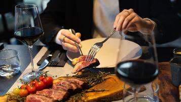 A dining table with a steak, tomatoes, and a glass of red wine.