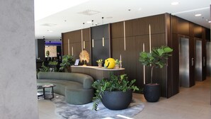 A modern lobby with a curved sofa, a reception desk, potted plants, and a wall-mounted elevator. - Radisson Blu Hotel, Hasselt (Hasselt)