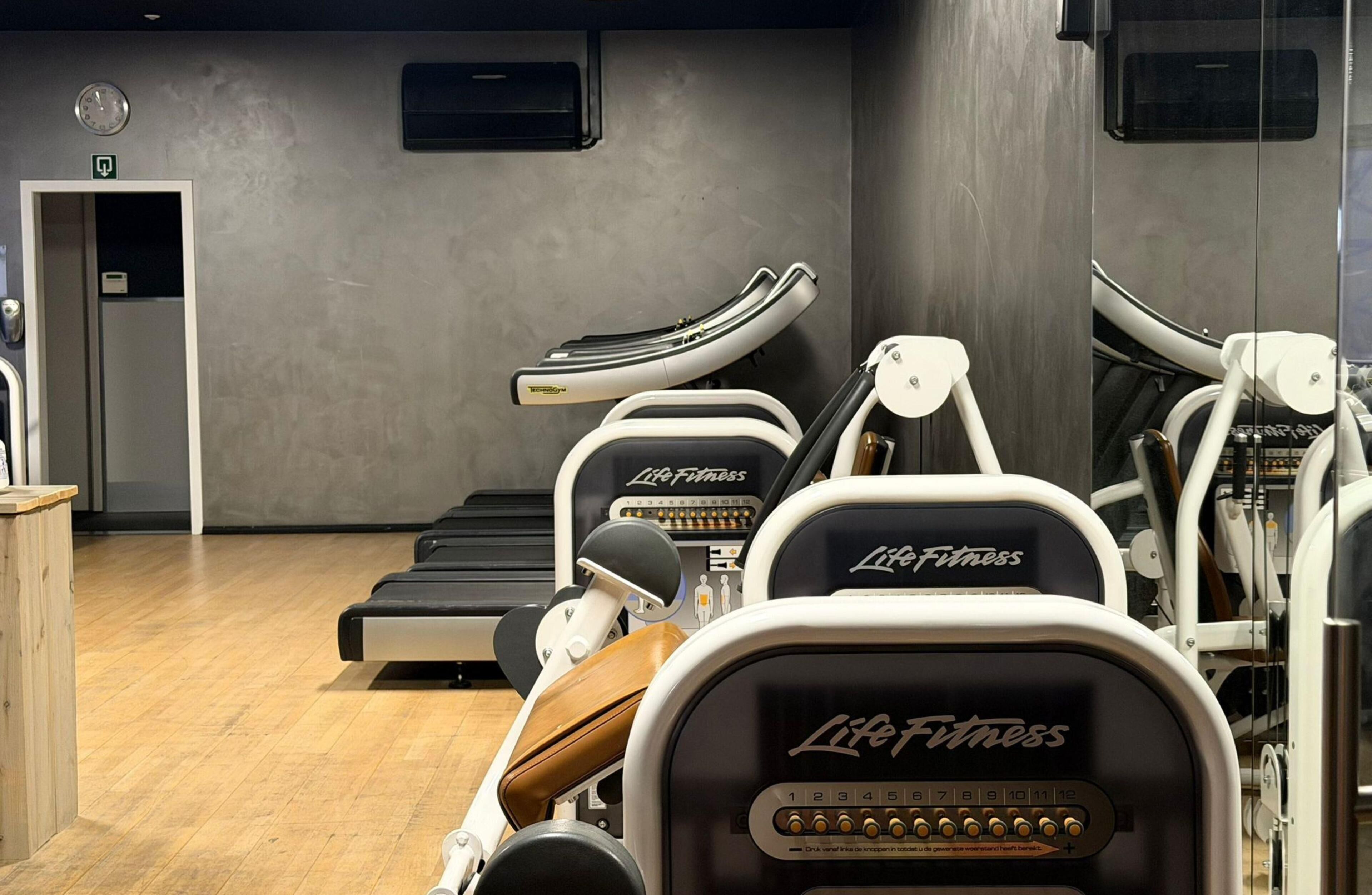 Une salle de sport équipée de tapis de course, d’appareils de musculation et dotée d’un plancher en bois.