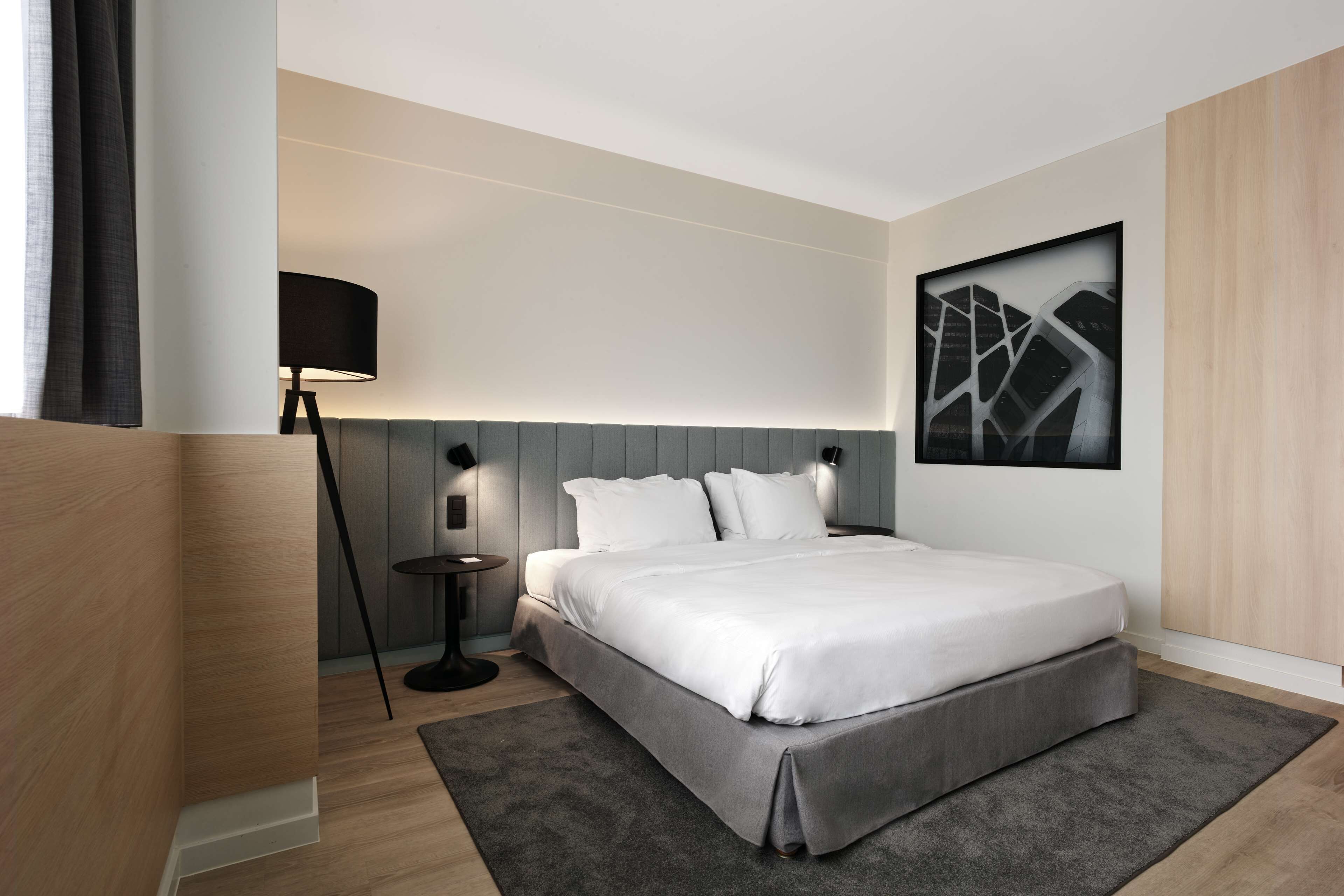Una habitación de hotel moderna con una cama grande, una mesita de noche, una lámpara y una obra de arte en la pared.