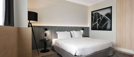 Una habitación de hotel moderna con una cama grande, una mesita de noche, una lámpara y una obra de arte en la pared.