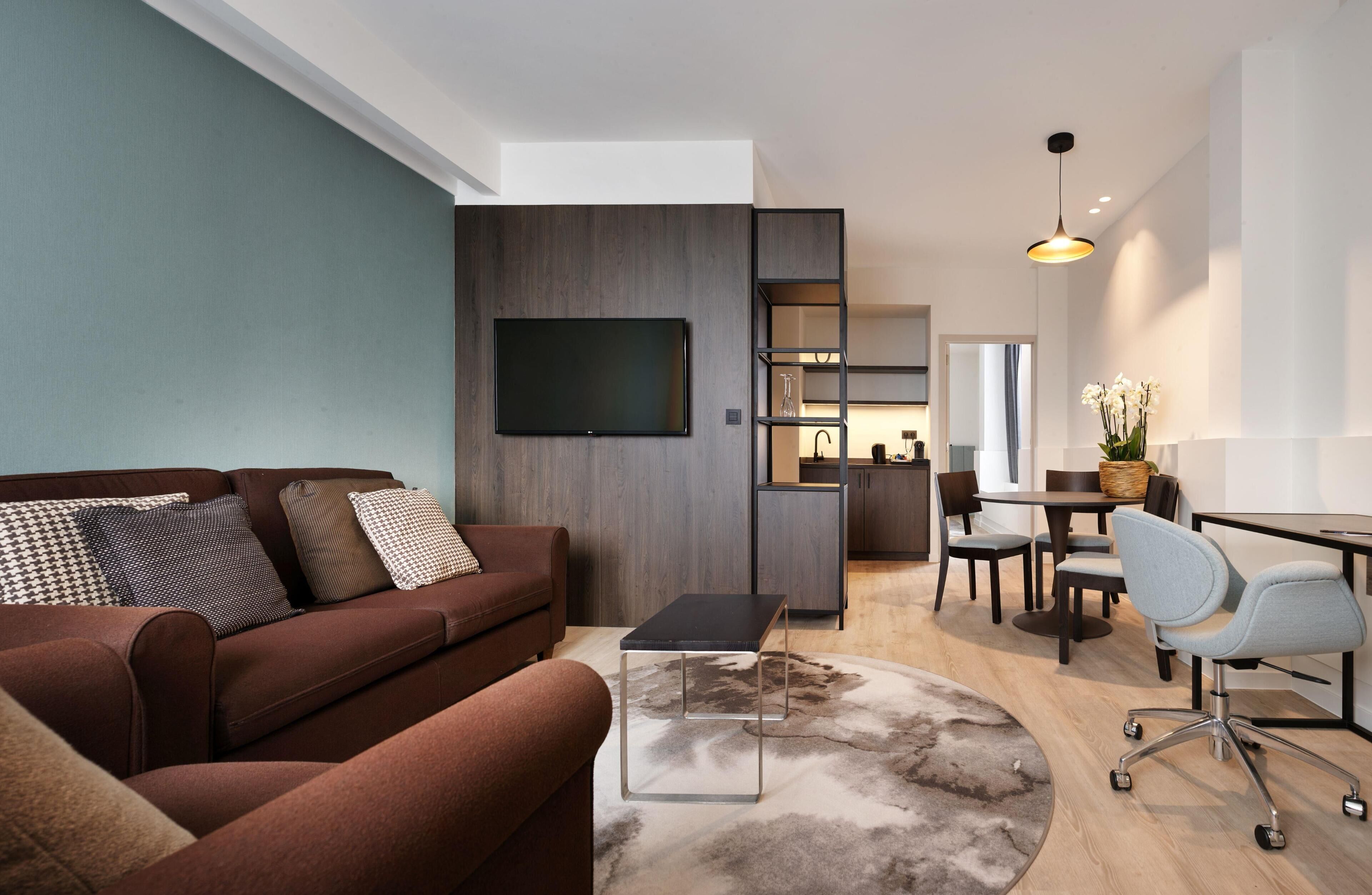 A modern living room with a sofa, a coffee table, a TV, and a dining area with chairs and a table.