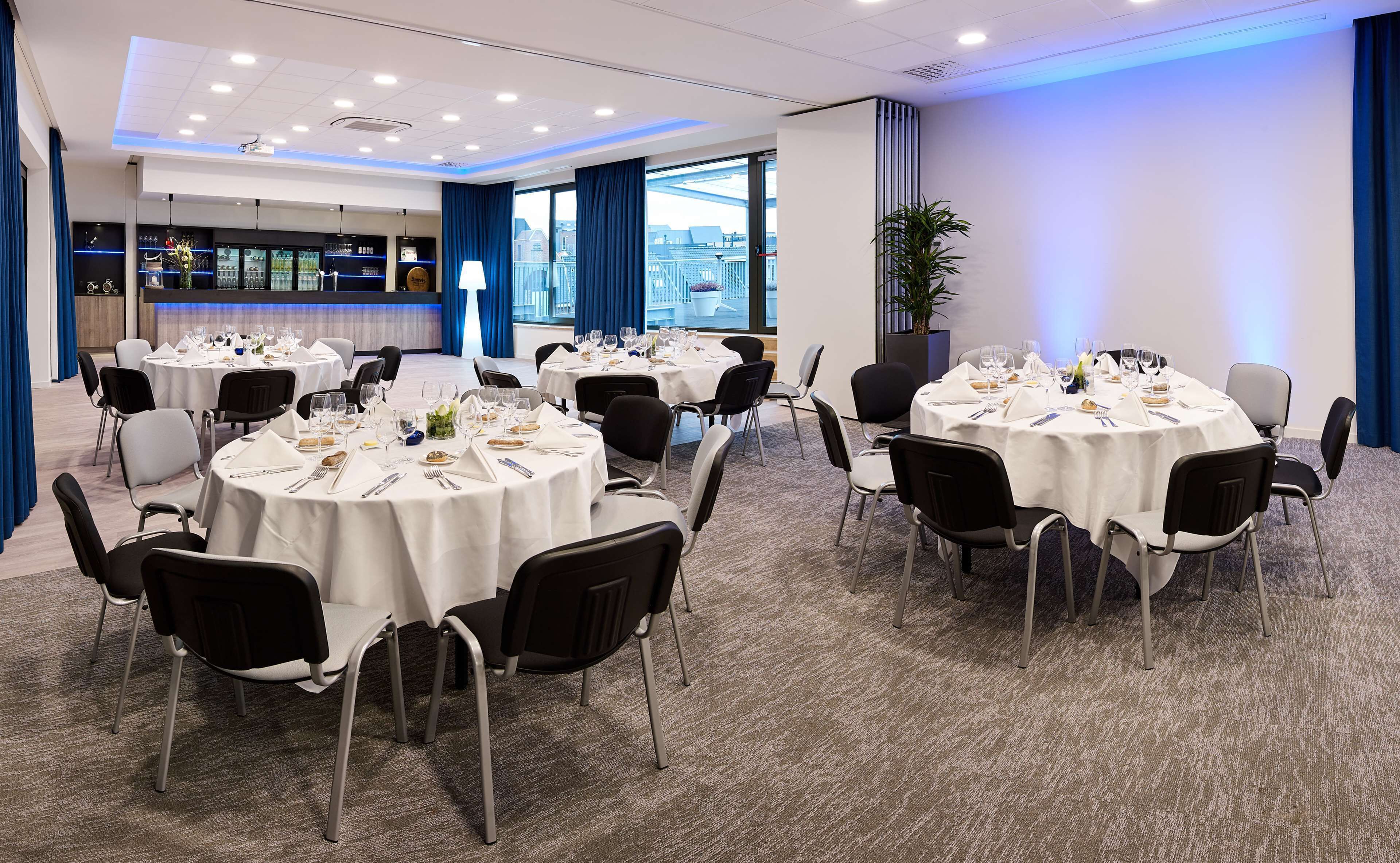 Ein Konferenzraum mit runden Tischen für das Essen, einer Bar und Blick auf die Stadtlandschaft.