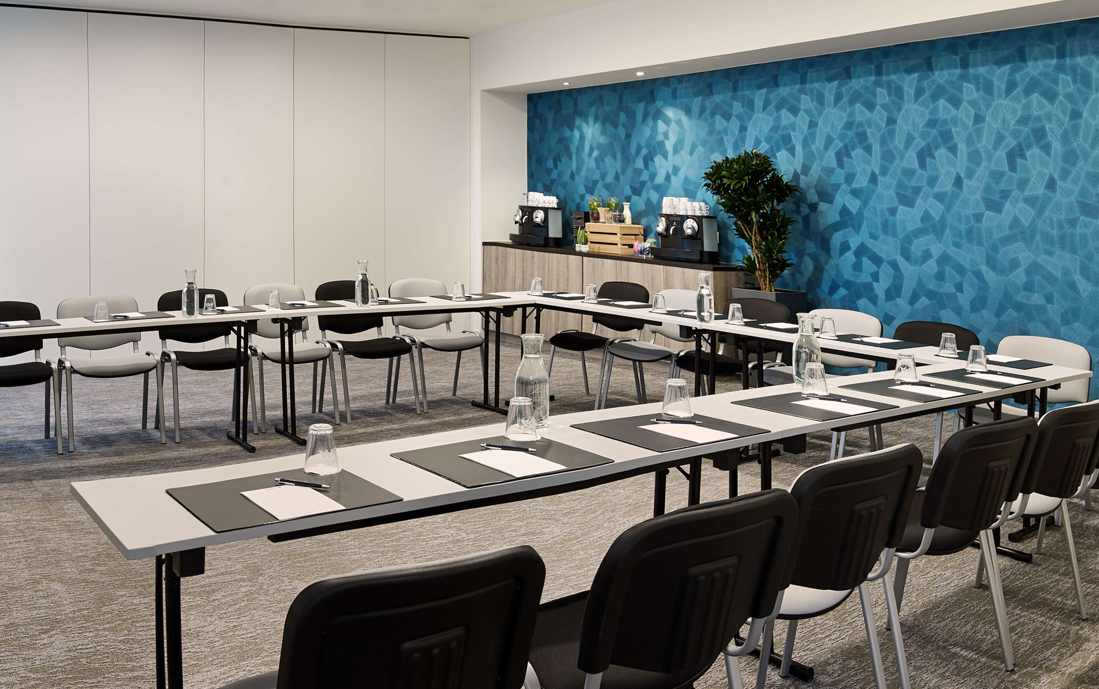 A conference room with a long table, chairs, water bottles, and a blue textured wall.