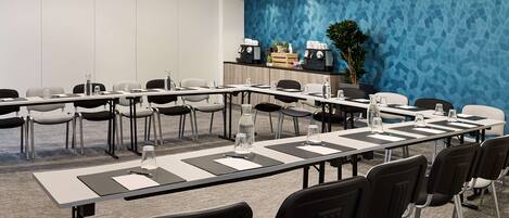 A conference room with a long table, chairs, water bottles, and a blue textured wall.