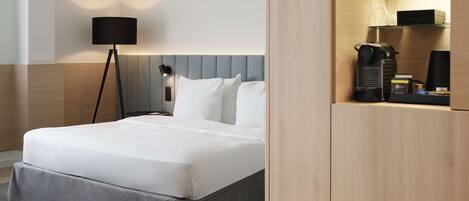 A neatly made bed with a grey skirt, a bedside lamp, and a nightstand with a lamp.