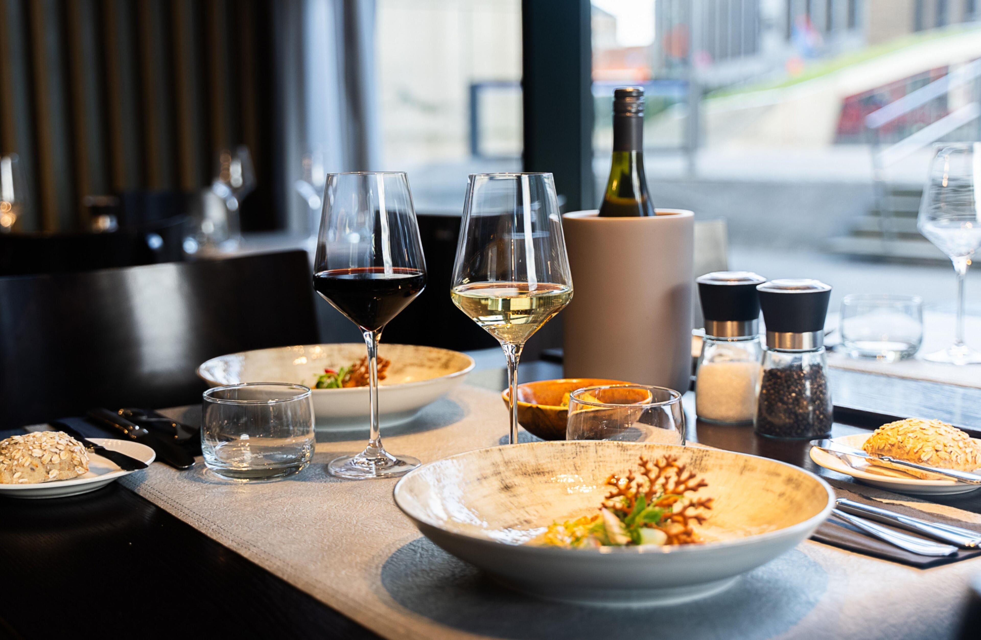 Une table à manger avec des assiettes remplies de nourriture, des verres de vin et une bouteille de vin.
