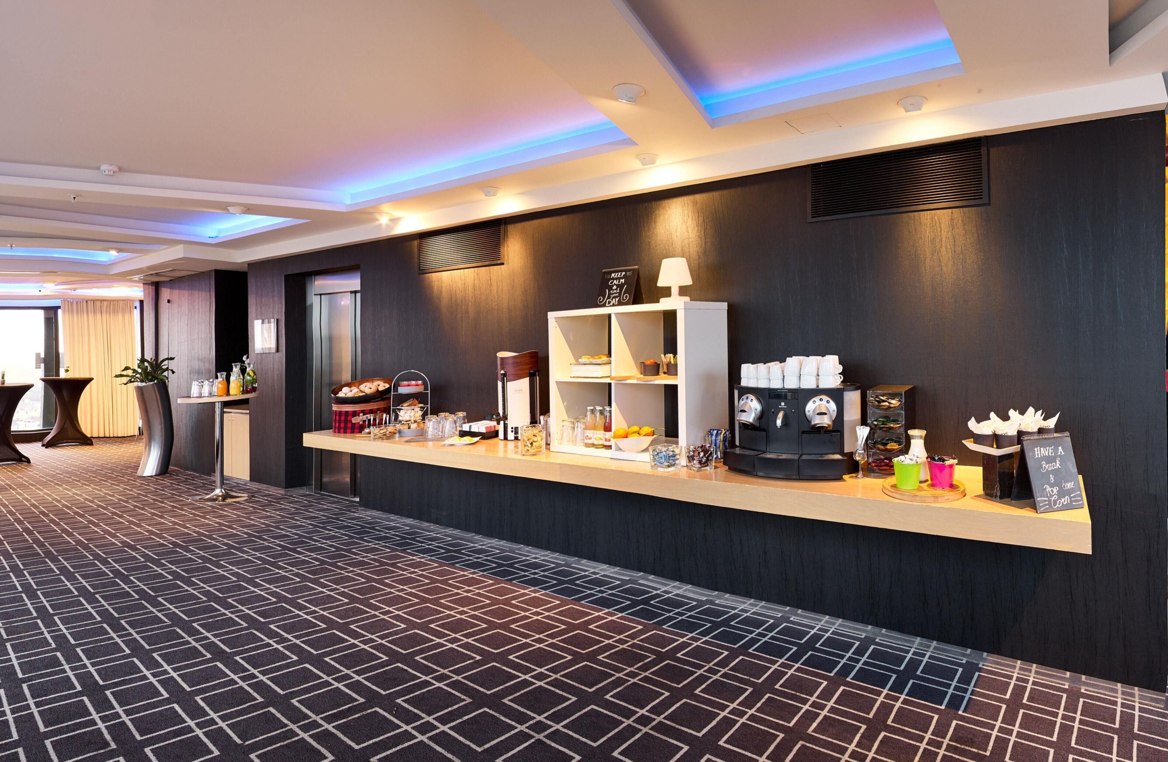 A modern hotel lobby with a reception desk, seating area, and a patterned carpet.