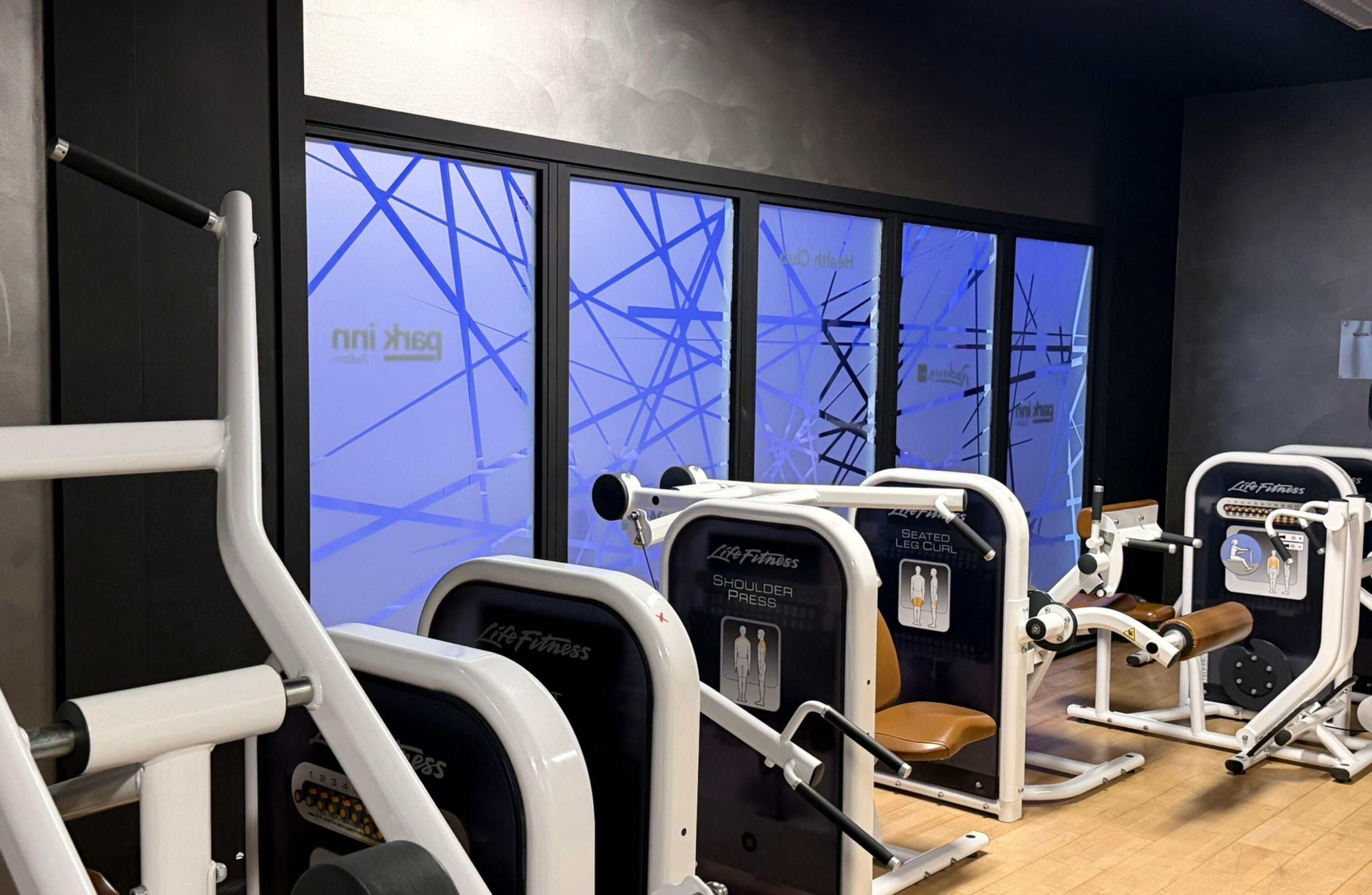 Een fitnessruimte met trainingsapparatuur, een groot raam met een blauw abstract ontwerp, en een zwarte muur.