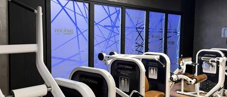 A gym with exercise equipment, a large window with a blue abstract design, and a black wall.