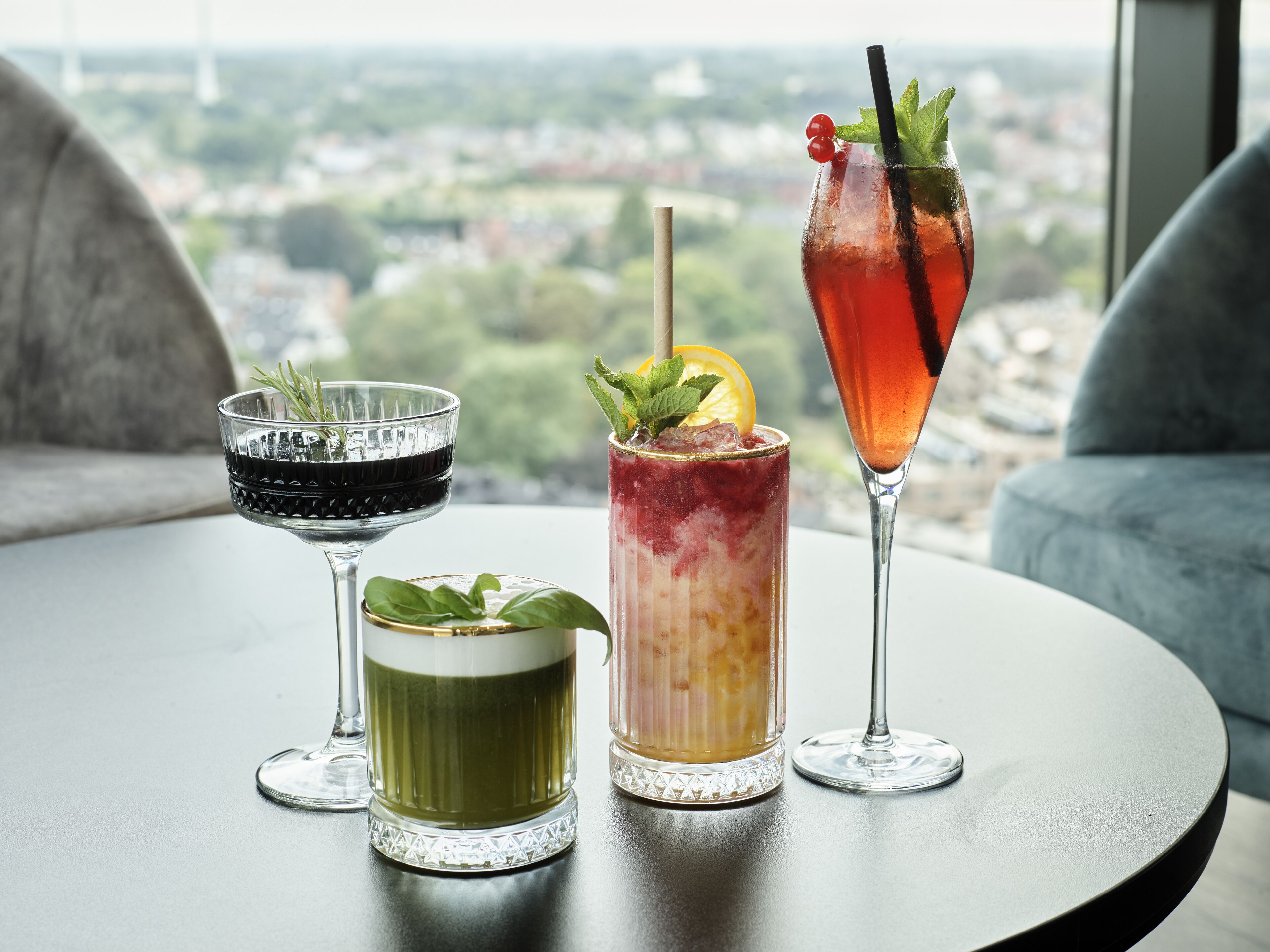 Three drinks on a table with a city view.