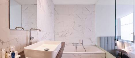 Un baño moderno con una bañera grande, un lavabo rectangular y un mueble de tocador con artículos de aseo.