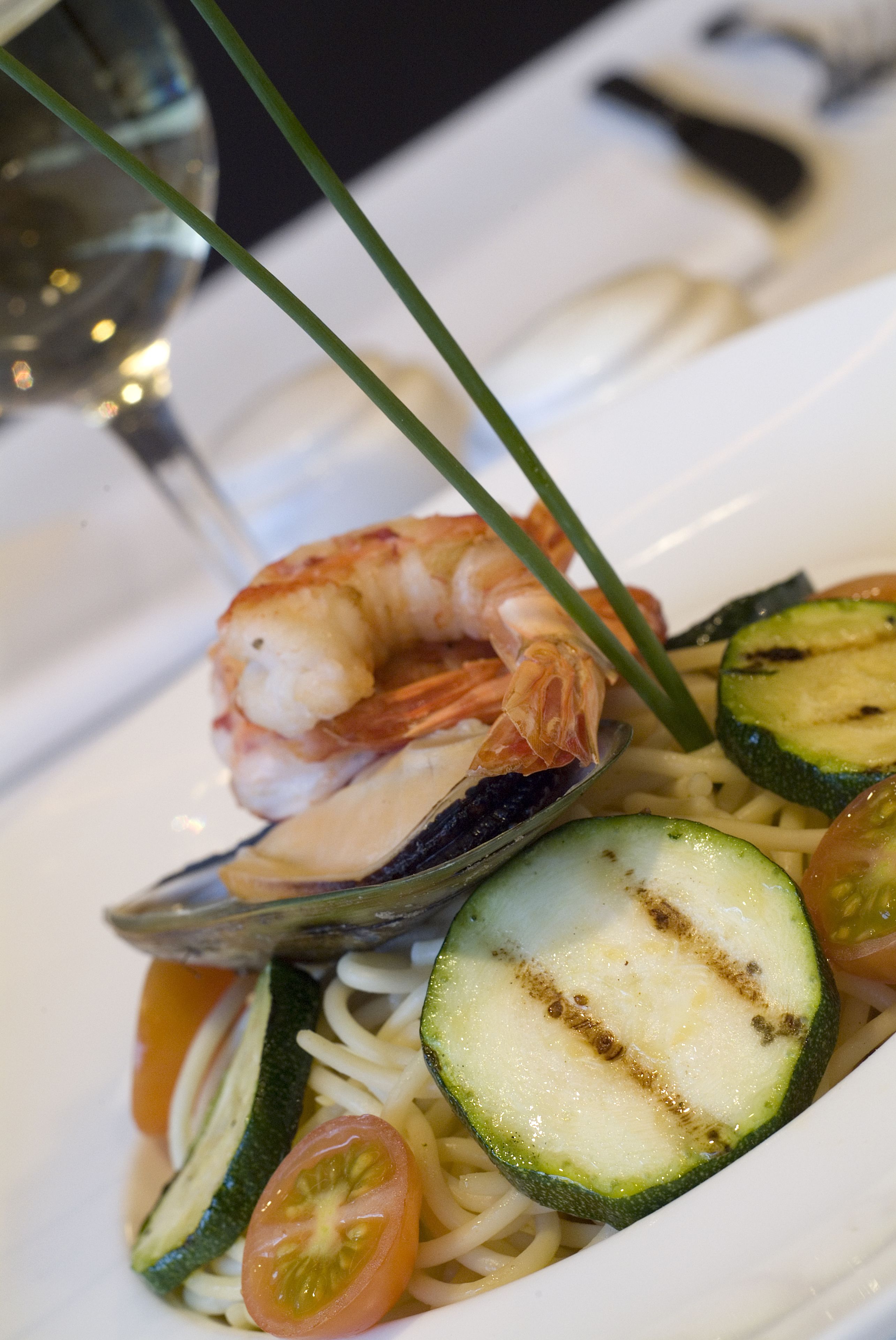 A plate of pasta with shrimp, clams, zucchini, and cherry tomatoes.