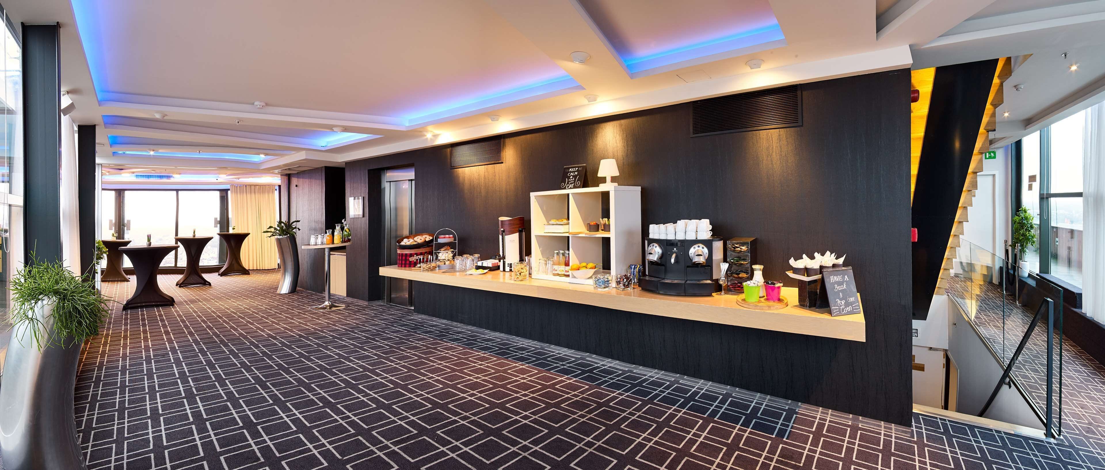 A modern hotel lobby with a reception desk, seating area, and a patterned carpet.