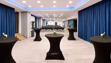 Ein Konferenzraum mit einem langen Tisch, schwarzen runden Tischen mit Vasen und blauen Vorhängen.