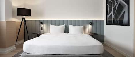 Een moderne hotelkamer met een groot bed, een staande vloerlamp, een bijzettafeltje en een ingelijst schilderij aan de muur.