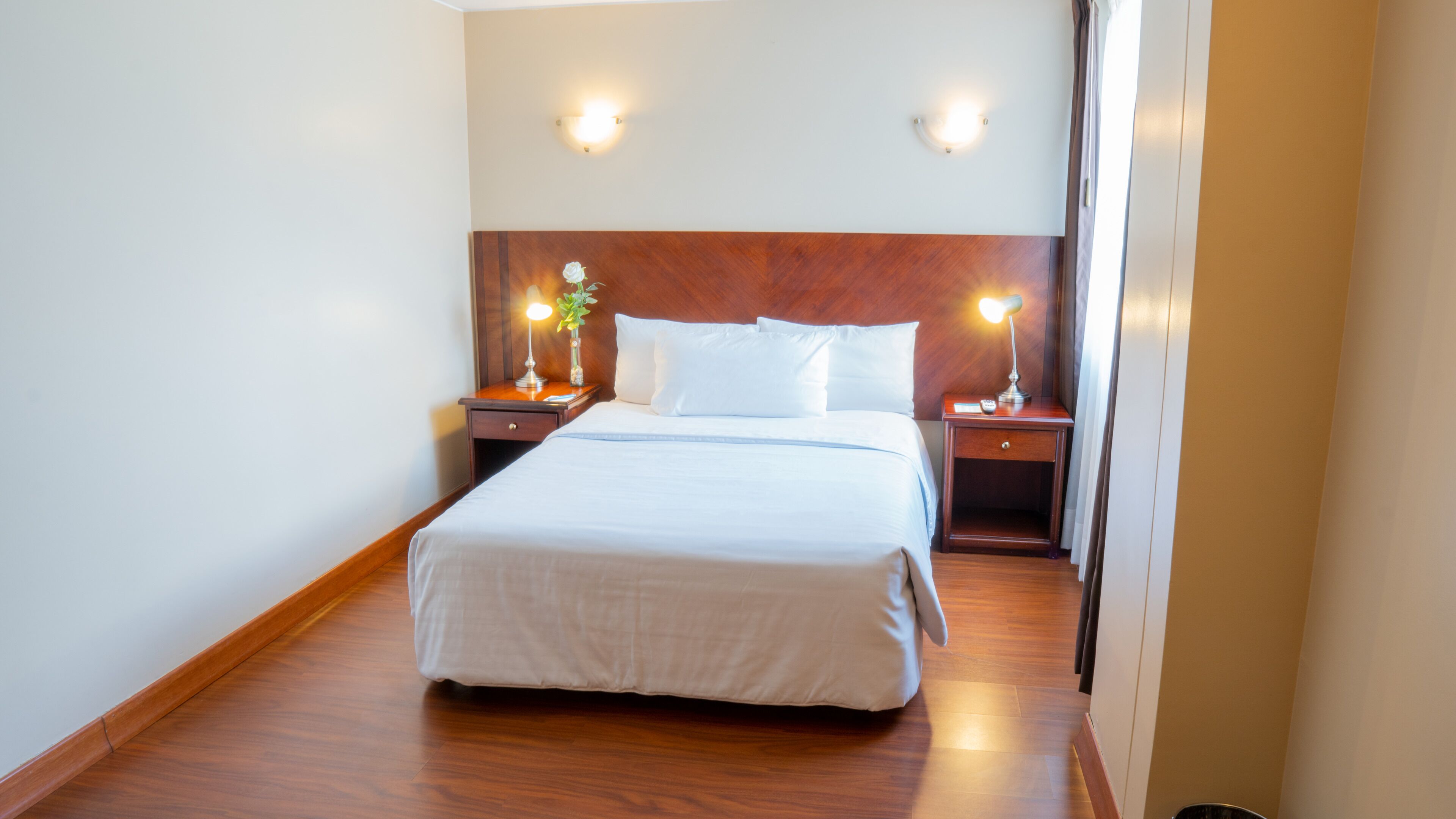 A hotel room with a large bed, two bedside tables, a nightstand, and two wall-mounted lights.