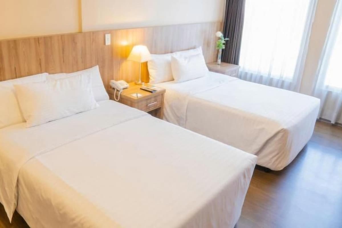 A hotel room with two beds, a nightstand with a lamp, and a window with curtains.