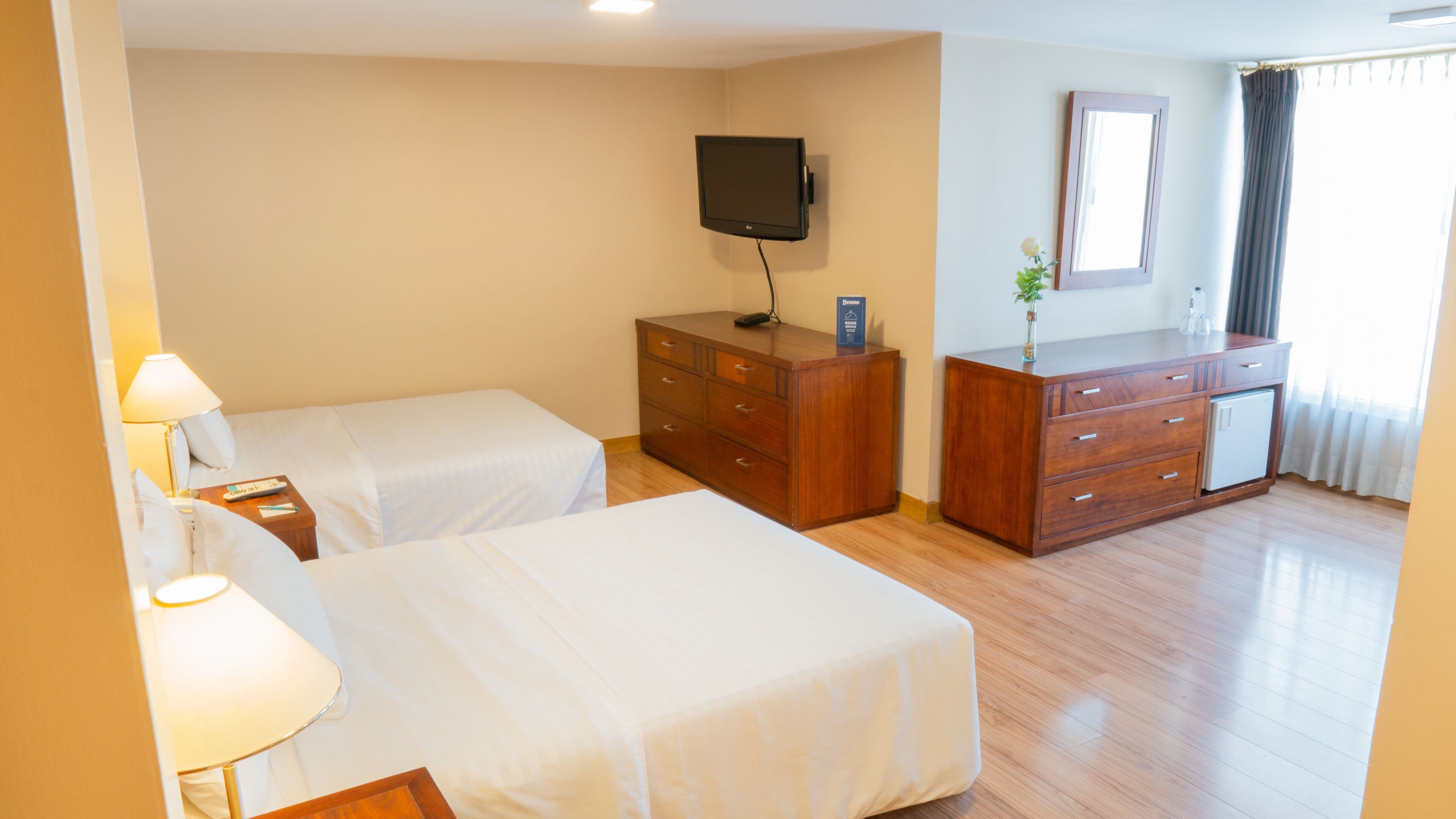 A hotel room with two beds, a dresser, a television, and a mirror.