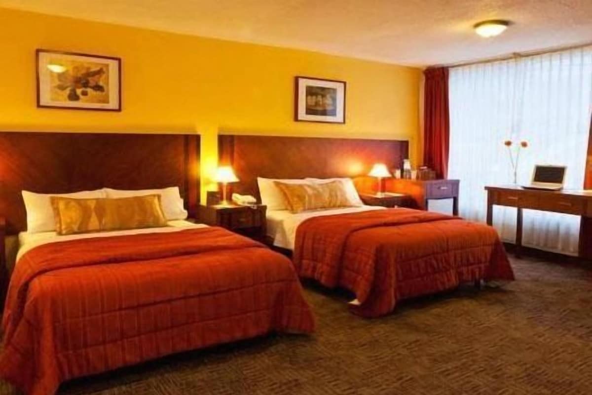 A hotel room with two beds, a desk, and a window with curtains.