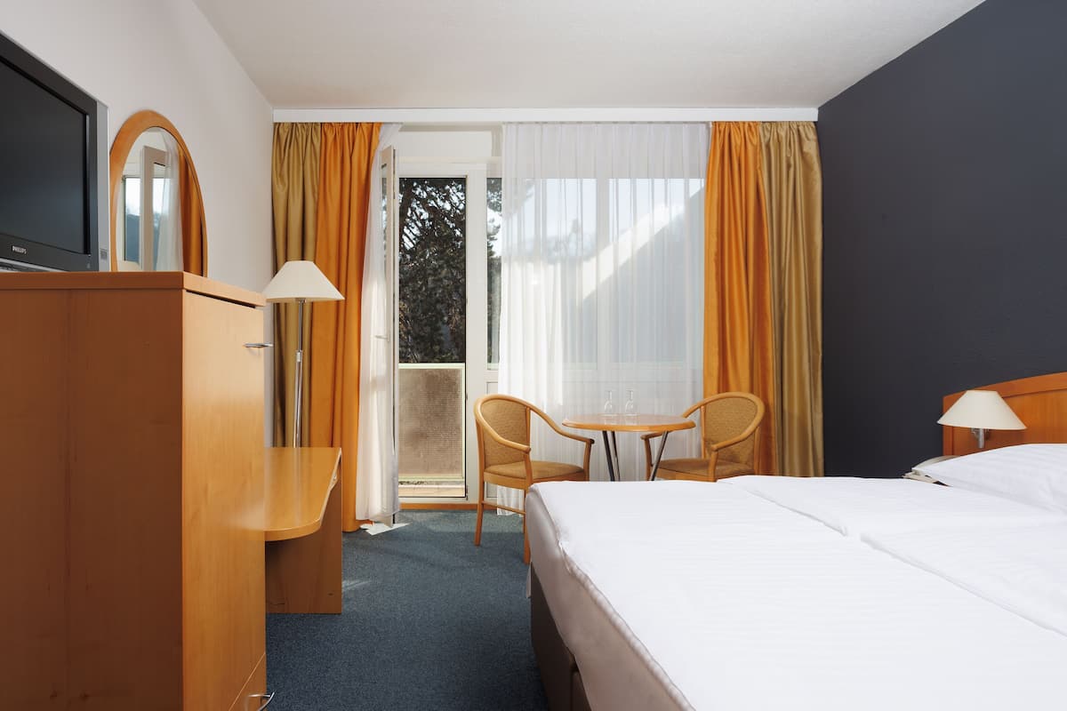 Hotelkamer met een bed, bureau, stoel, televisie en raam met gordijnen.