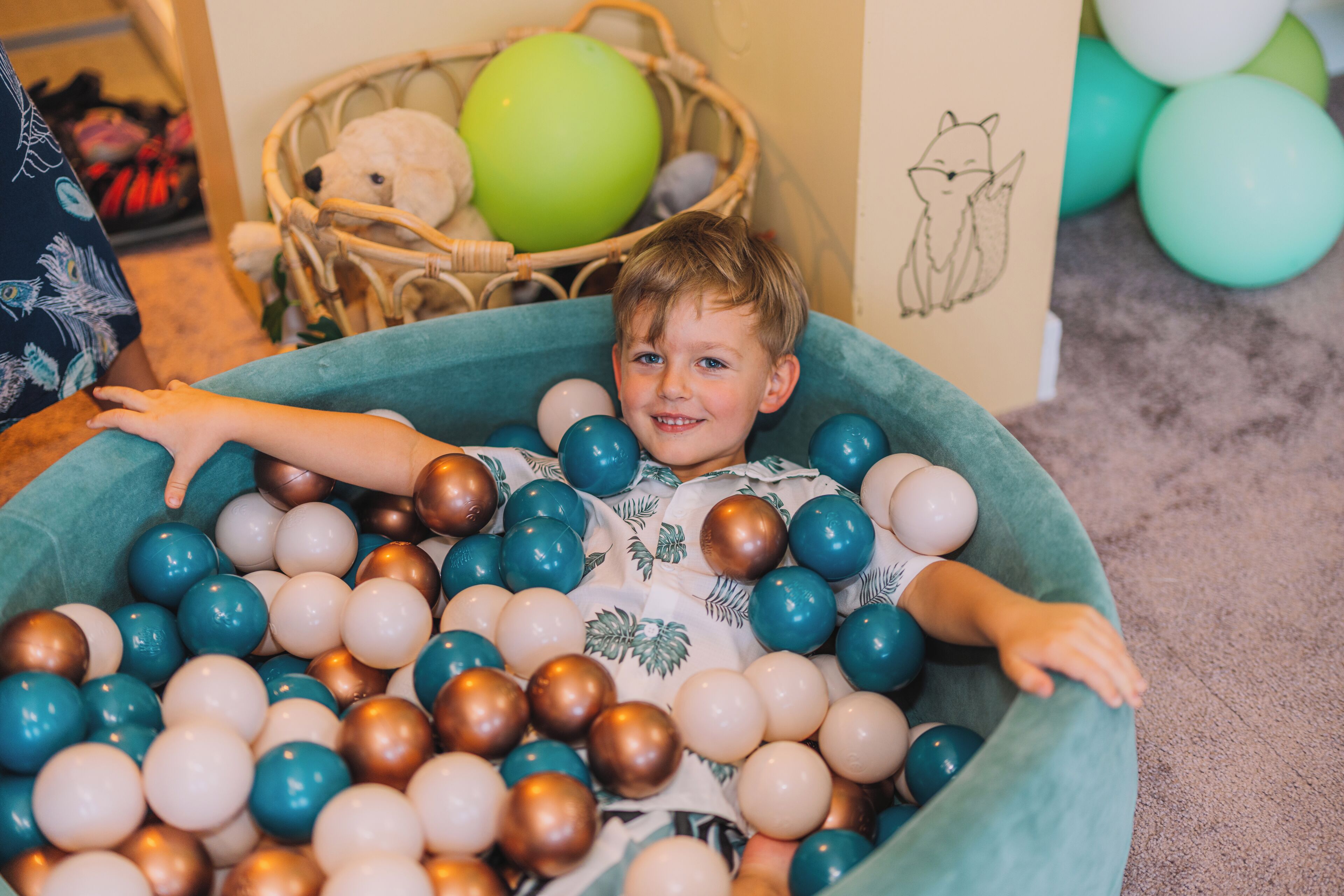 Een kind zit in een bällebak vol kleurrijke ballen.