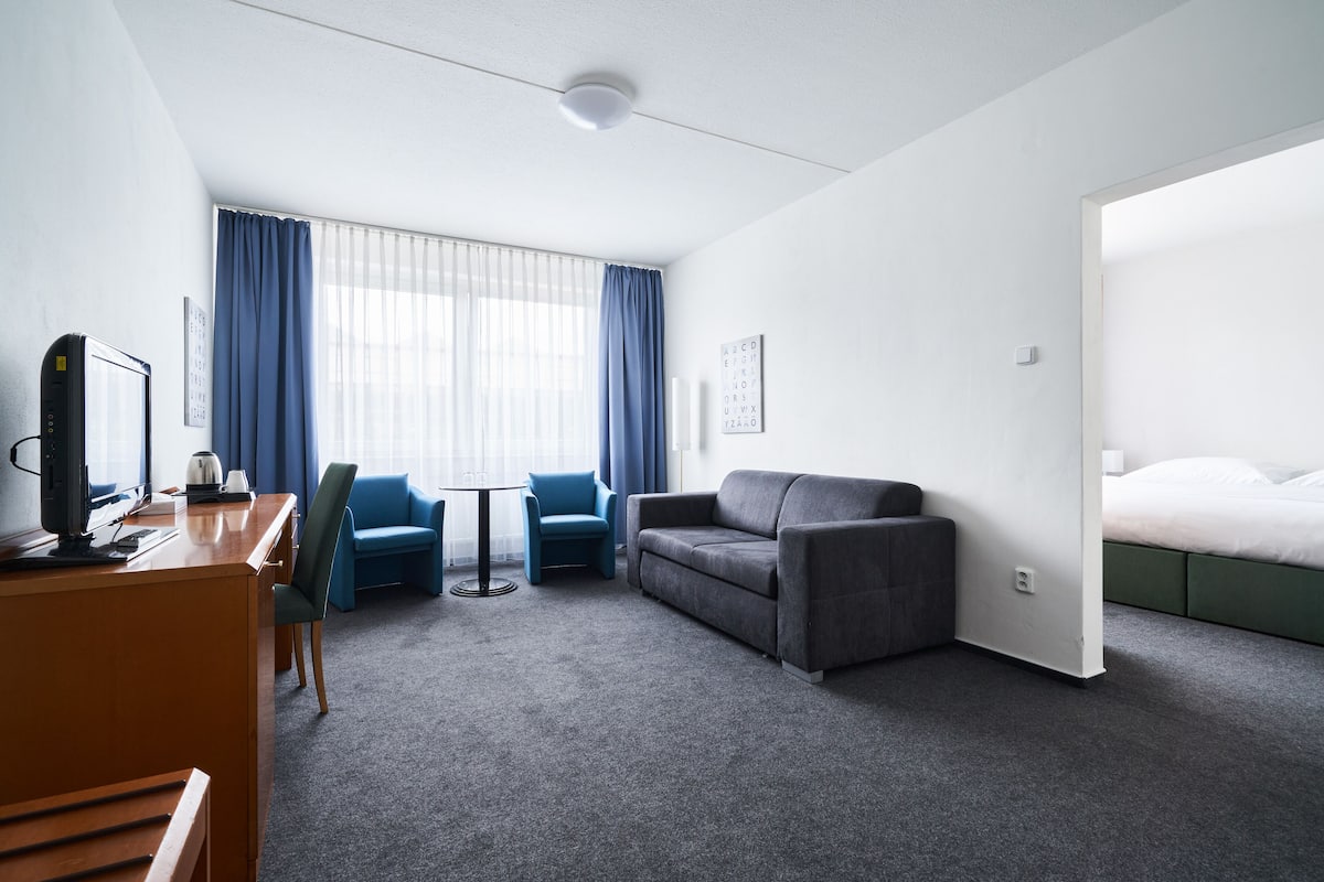 Hotelkamer met bureau, twee stoelen, een bank, een bed en een raam met gordijnen.