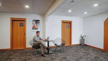 Een man zittend aan een tafel met een laptop in een kamer met twee deuren, de deuren zijn gelabeld 'Office', een vloerbedekking en een bord met een gebied waar niet gelopen mag worden.
