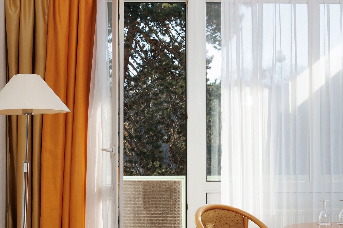 Une chambre d’hôtel avec un lit, une chaise, une table, une lampe et une vue sur les arbres par la fenêtre.