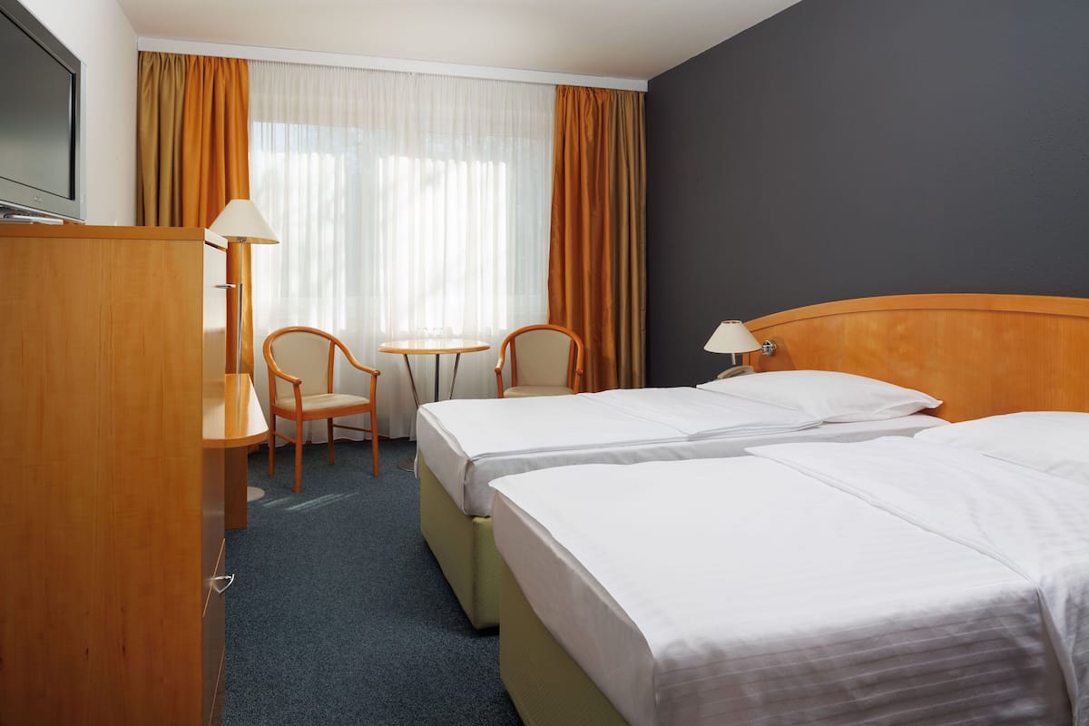 Een hotelkamer met twee bedden, een bureau met een televisie, een kleine tafel, twee stoelen en een raam met gordijnen.