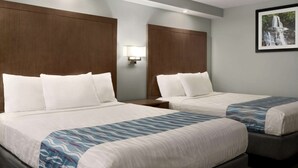 A hotel room with two beds, each with white bedding and a blue patterned throw. There is a wall-mounted lamp between the beds and a framed picture of a waterfall on the wall. - Gatlinburg River Inn (Gatlinburg)