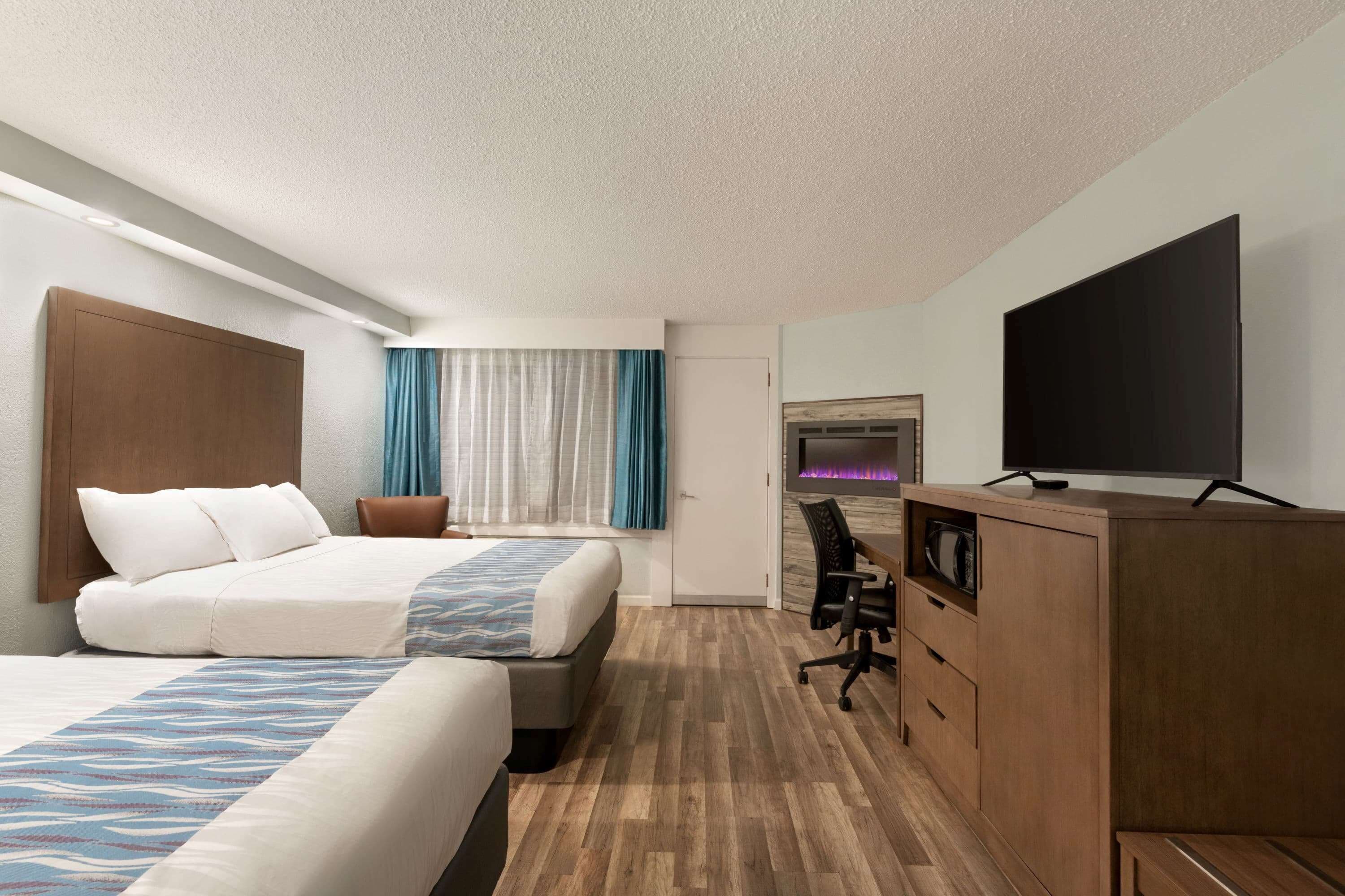 A hotel room with two beds, a desk, a television, and a minibar.