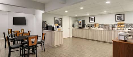 A modern kitchen with a central island, a dining area with wooden chairs, and a flat-screen TV mounted on the wall.