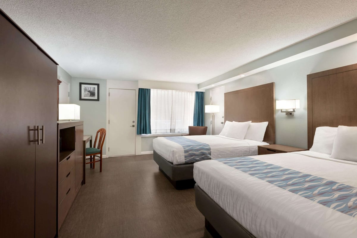 Une chambre d’hôtel avec deux lits, un bureau, une chaise et une armoire.