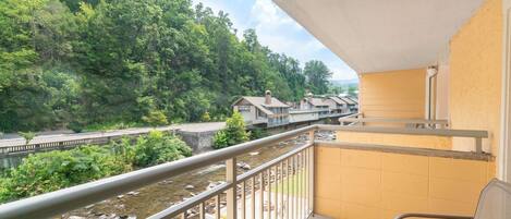 Ein Balkon mit Blick auf einen Fluss und bewaldetes Gebiet, ein Stuhl und ein Gebäude mit einem Schild.