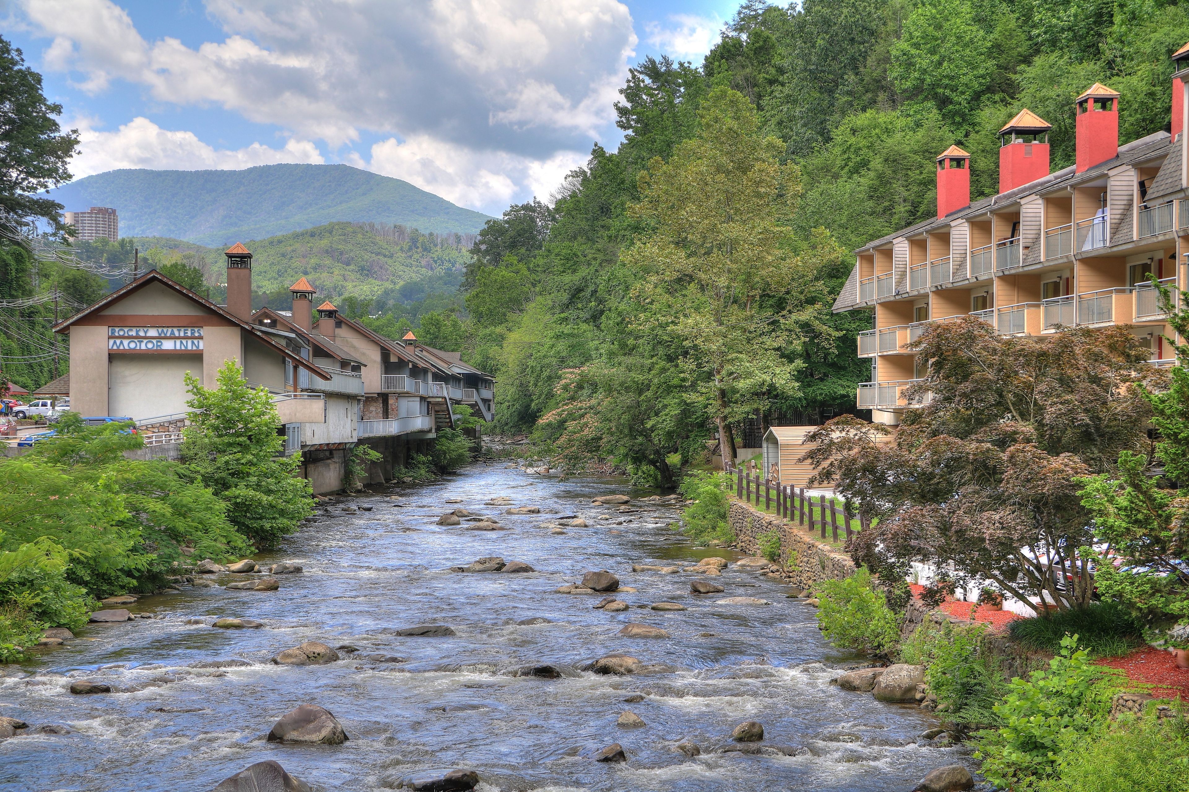 Une rivière bordée de rochers, entourée de verdure et de bâtiments, notamment un motel et un hôtel doté de balcons.