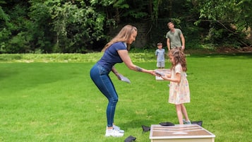 Una mujer enseñando a un niño a jugar tenis de mesa al aire libre sobre un campo de césped.