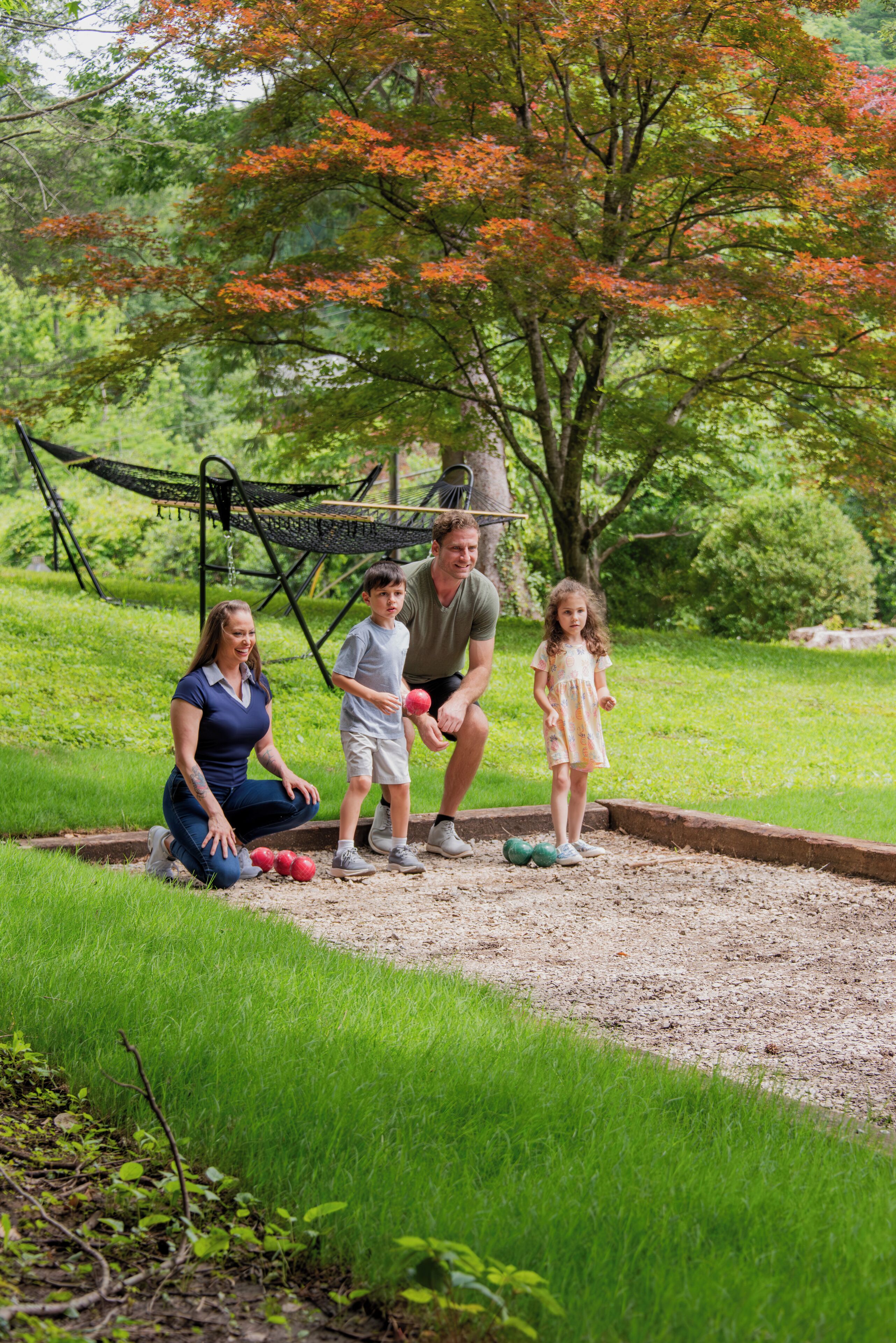 A family of four in a park with a hammock and a tree with orange leaves.