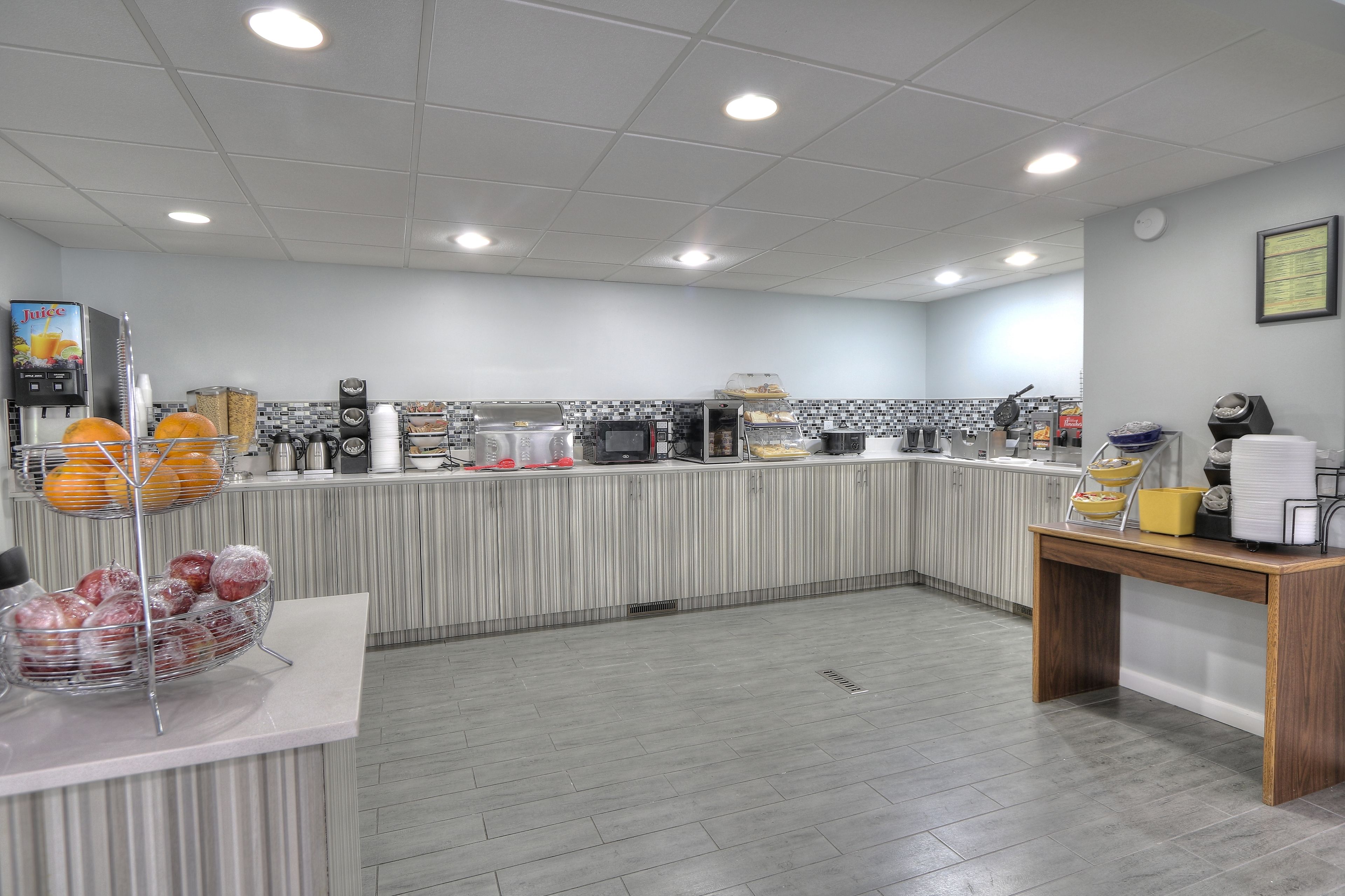 A modern kitchen with a counter, various appliances, and a display of fruits and vegetables.