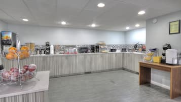 A modern kitchen with a counter, various appliances, and a display of fruits and vegetables.