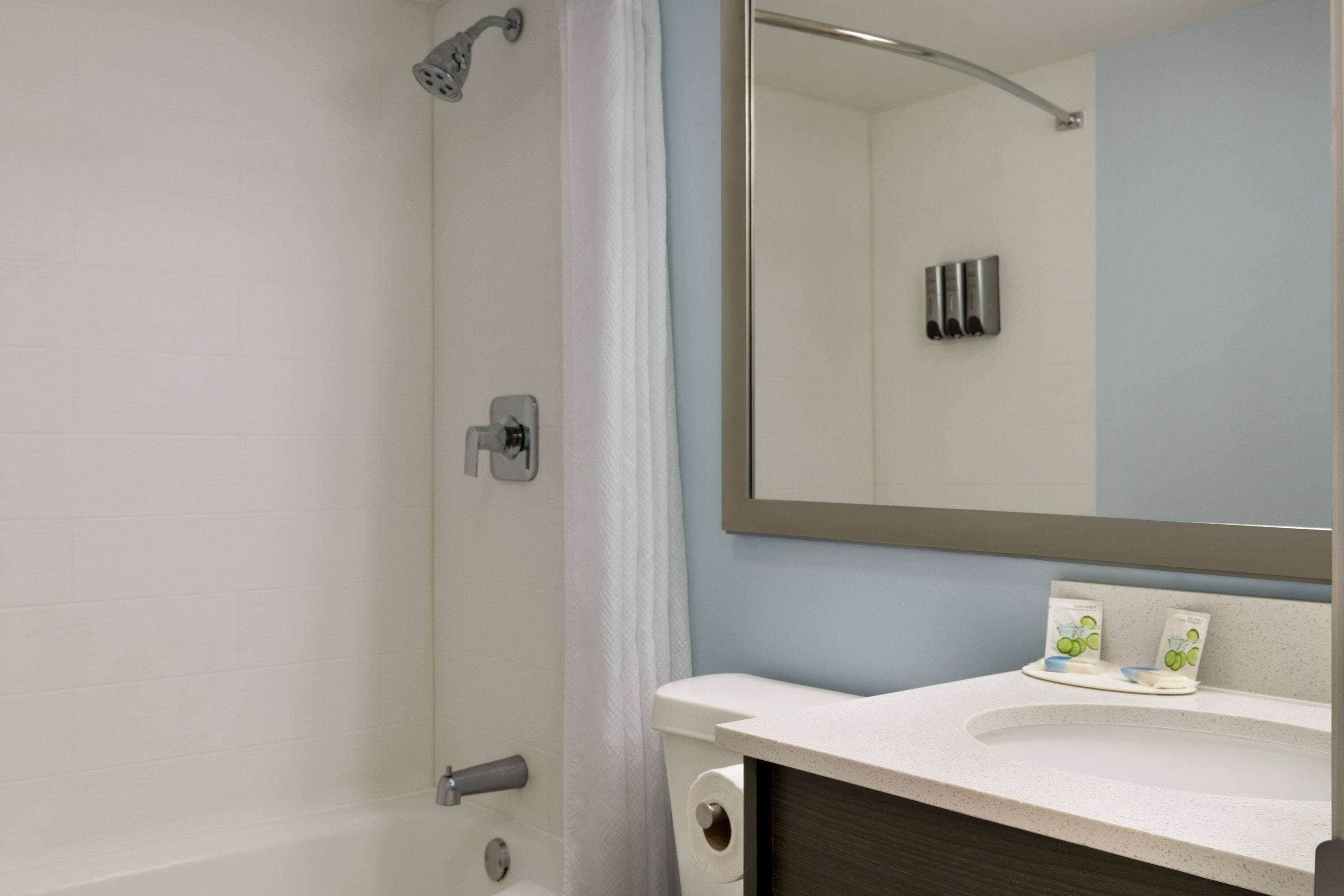 A bathroom with a shower, toilet, sink, and mirror.
