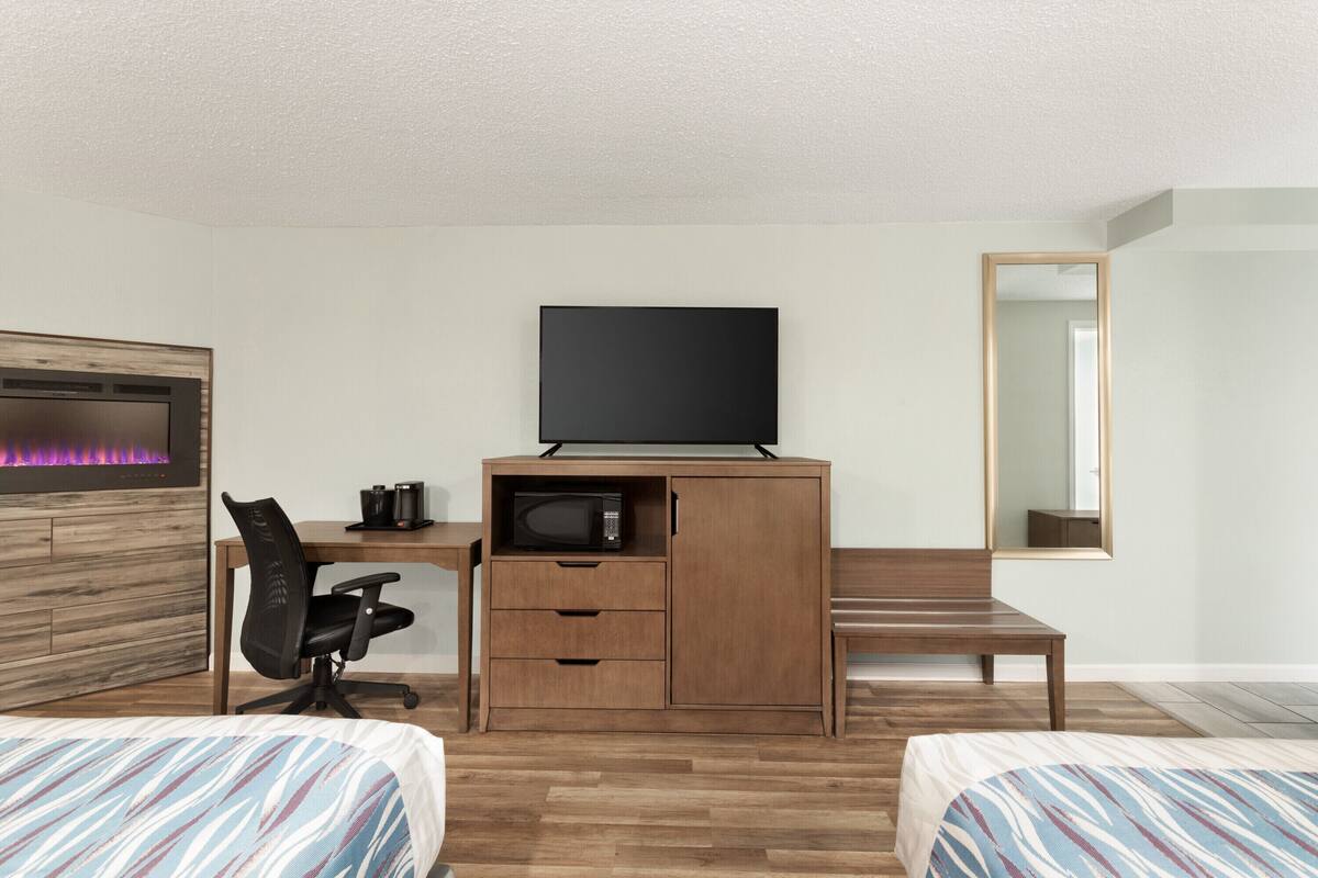 Une chambre d’hôtel équipée d’un bureau en bois, d’une télévision, d’un four à micro-ondes, d’une chaise et de deux lits.