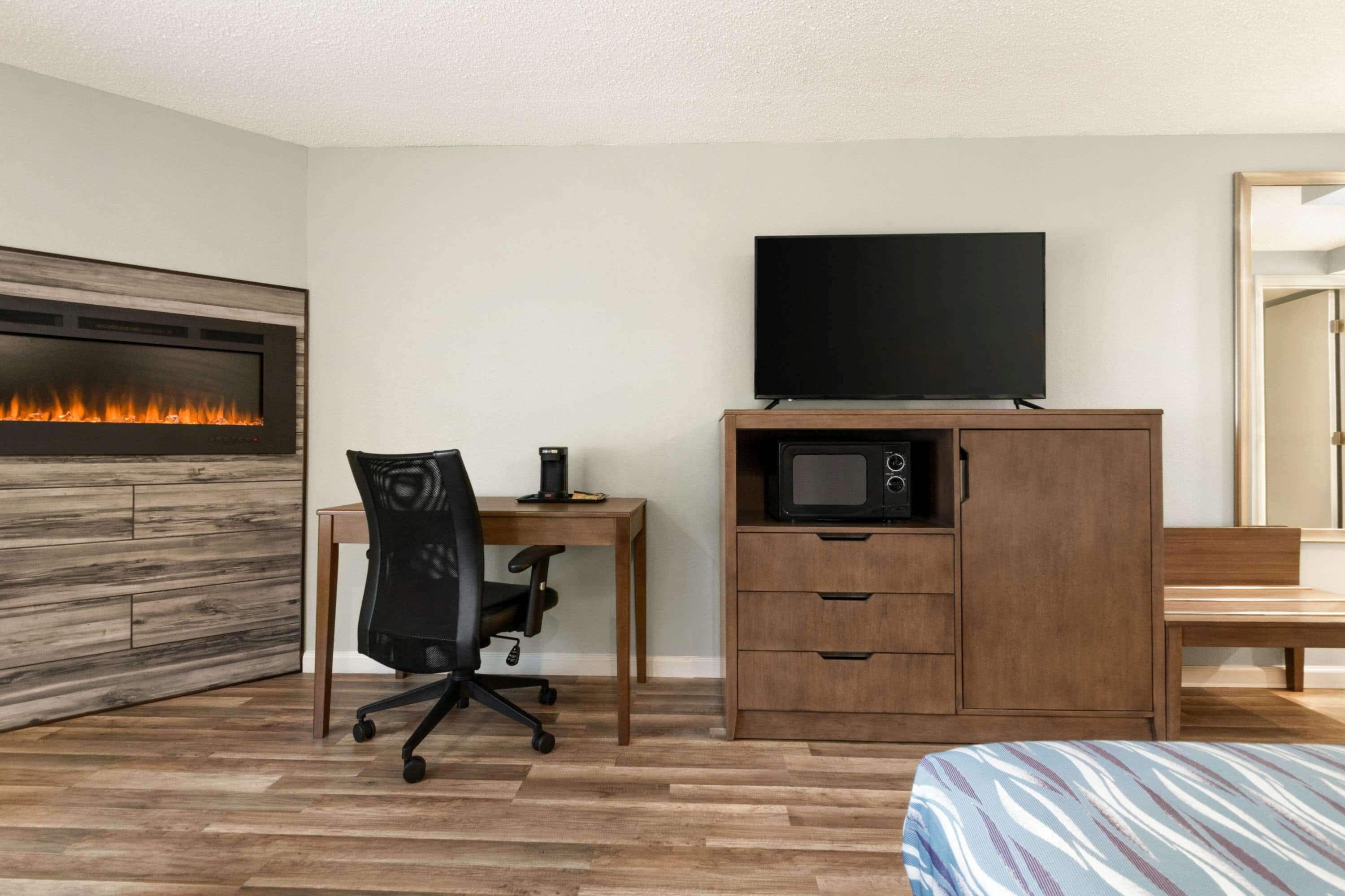 A hotel room with a wood-paneled fireplace, a television, a microwave, a desk with a chair, and a bed with striped bedding.