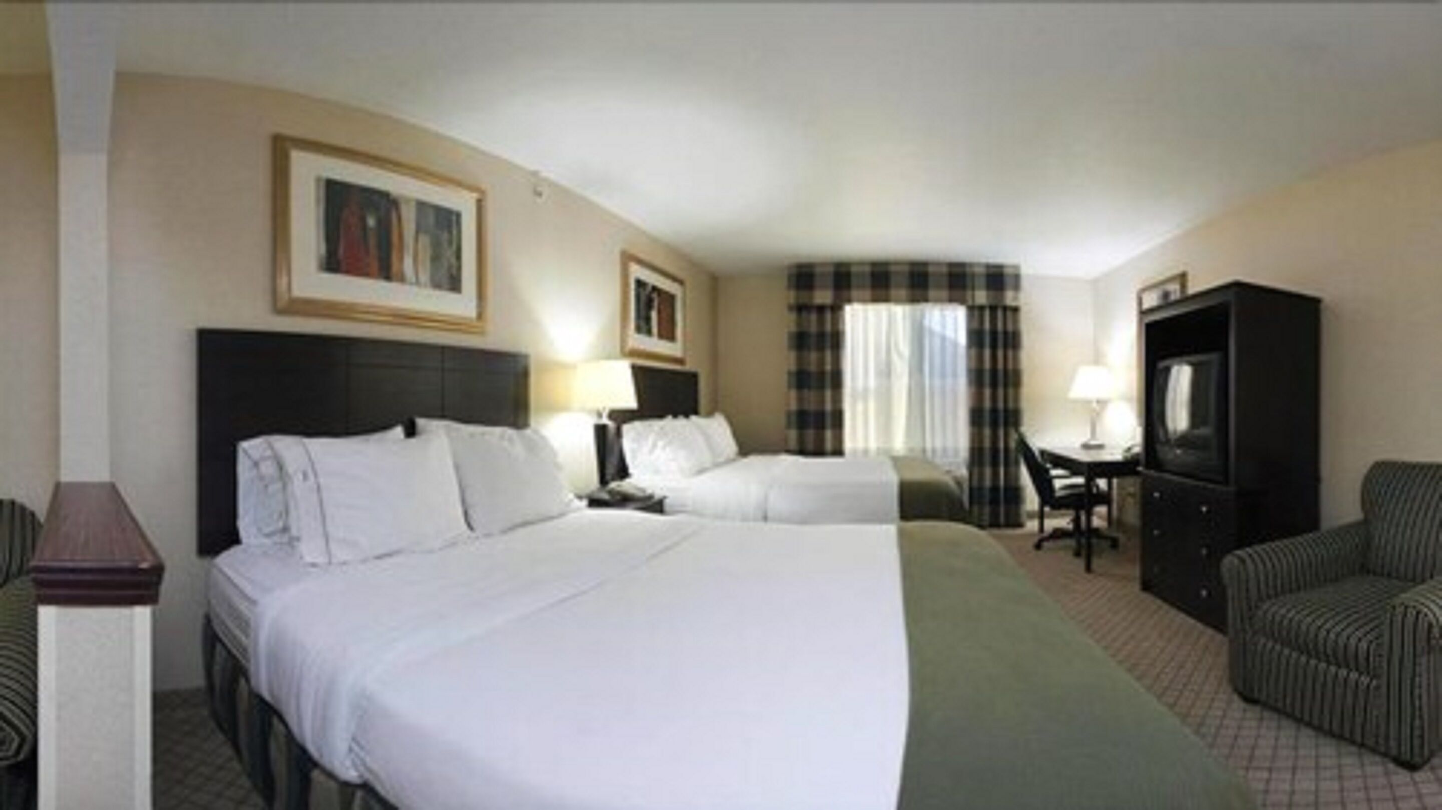 A hotel room with two beds, a desk, a television, and a chair.