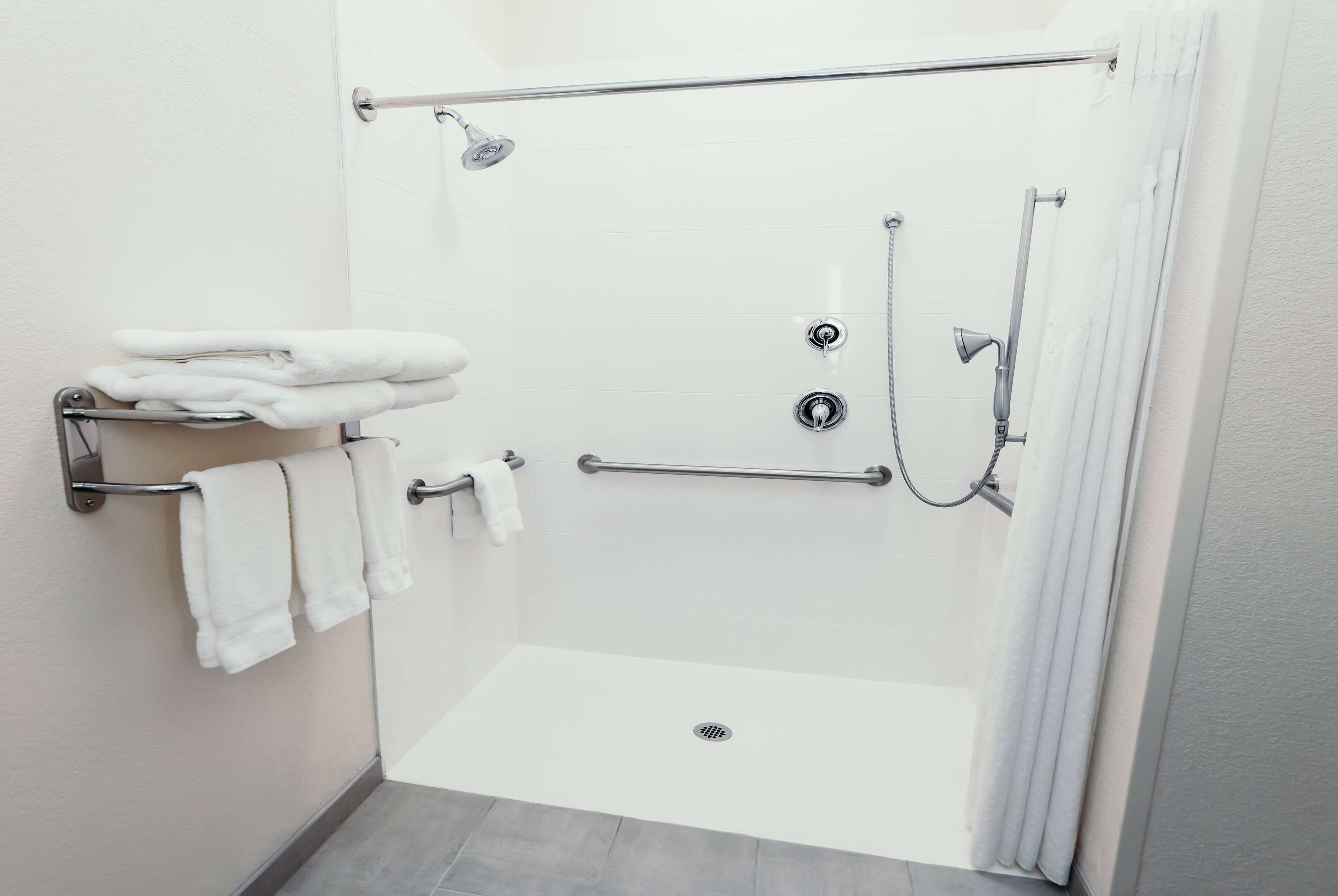 A modern shower area with a glass door, grab bars, and a towel rack.