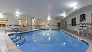 A large indoor swimming pool with clear water, surrounded by lounge chairs and a small seating area.