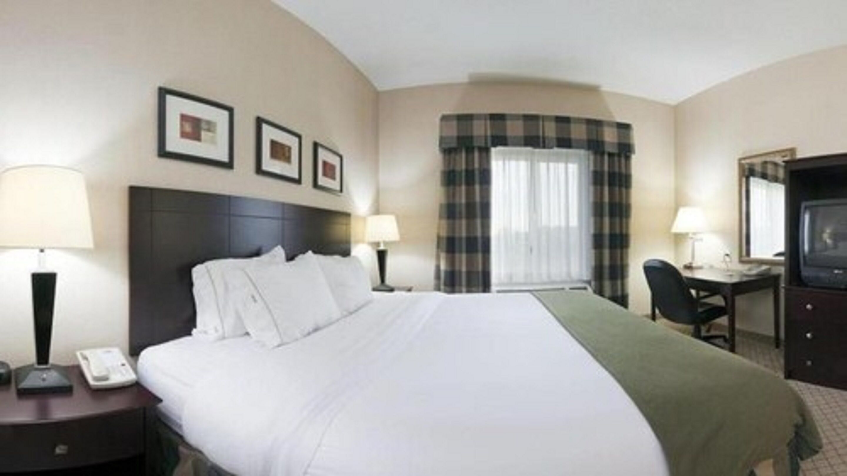 A hotel room with a large bed, two bedside tables with lamps, a desk with a chair, a television, and a window with curtains.