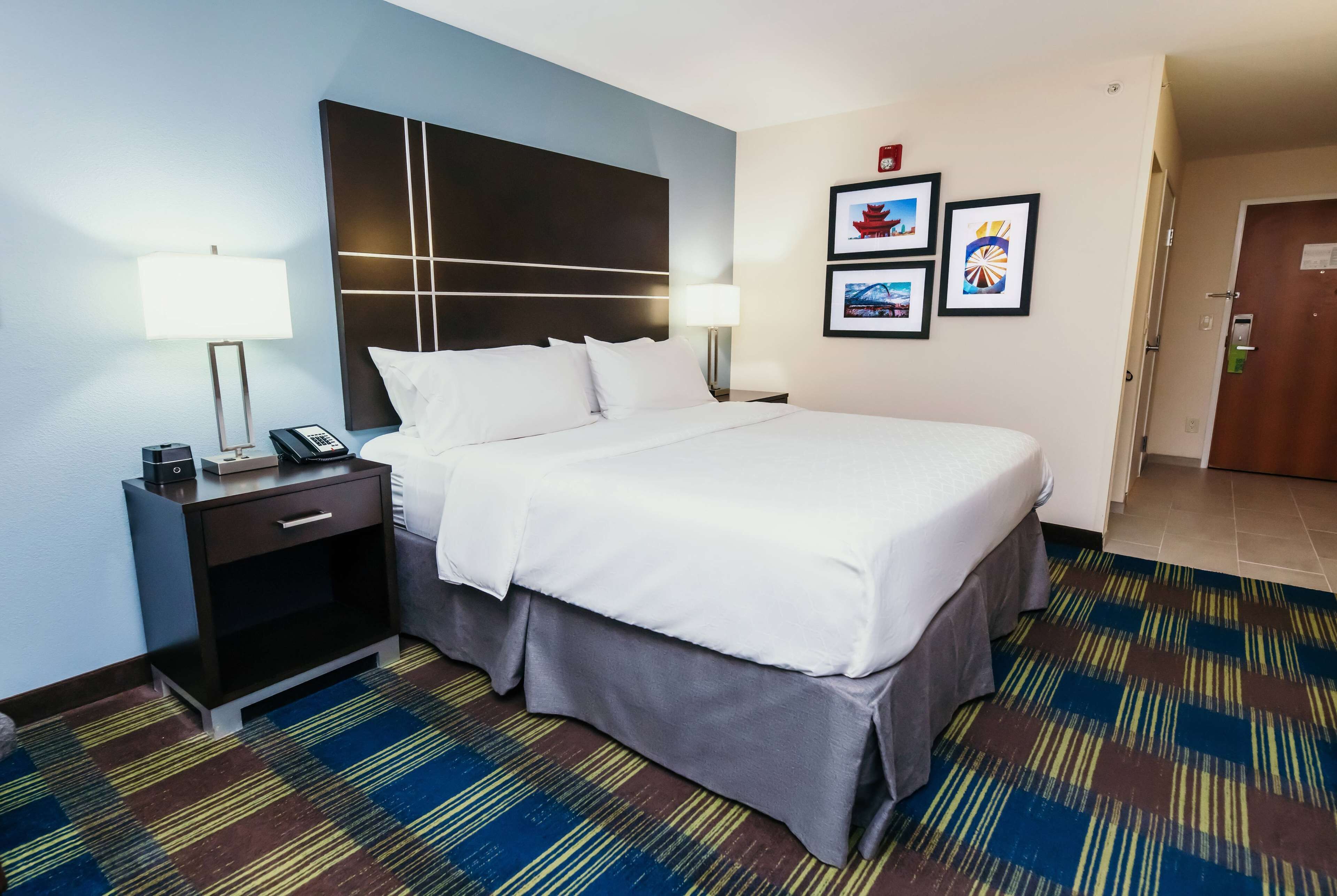 A hotel room with a large bed, a nightstand with a lamp, and a wall-mounted phone.