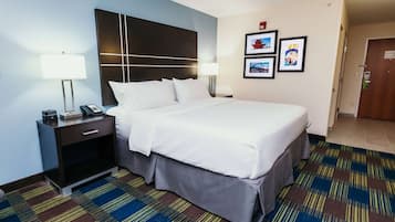 A hotel room with a large bed, a nightstand with a lamp, and a wall-mounted phone.