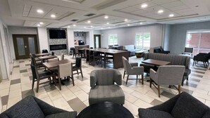A spacious indoor area with multiple seating arrangements, including tables and chairs, a sofa, and a television mounted on the wall.